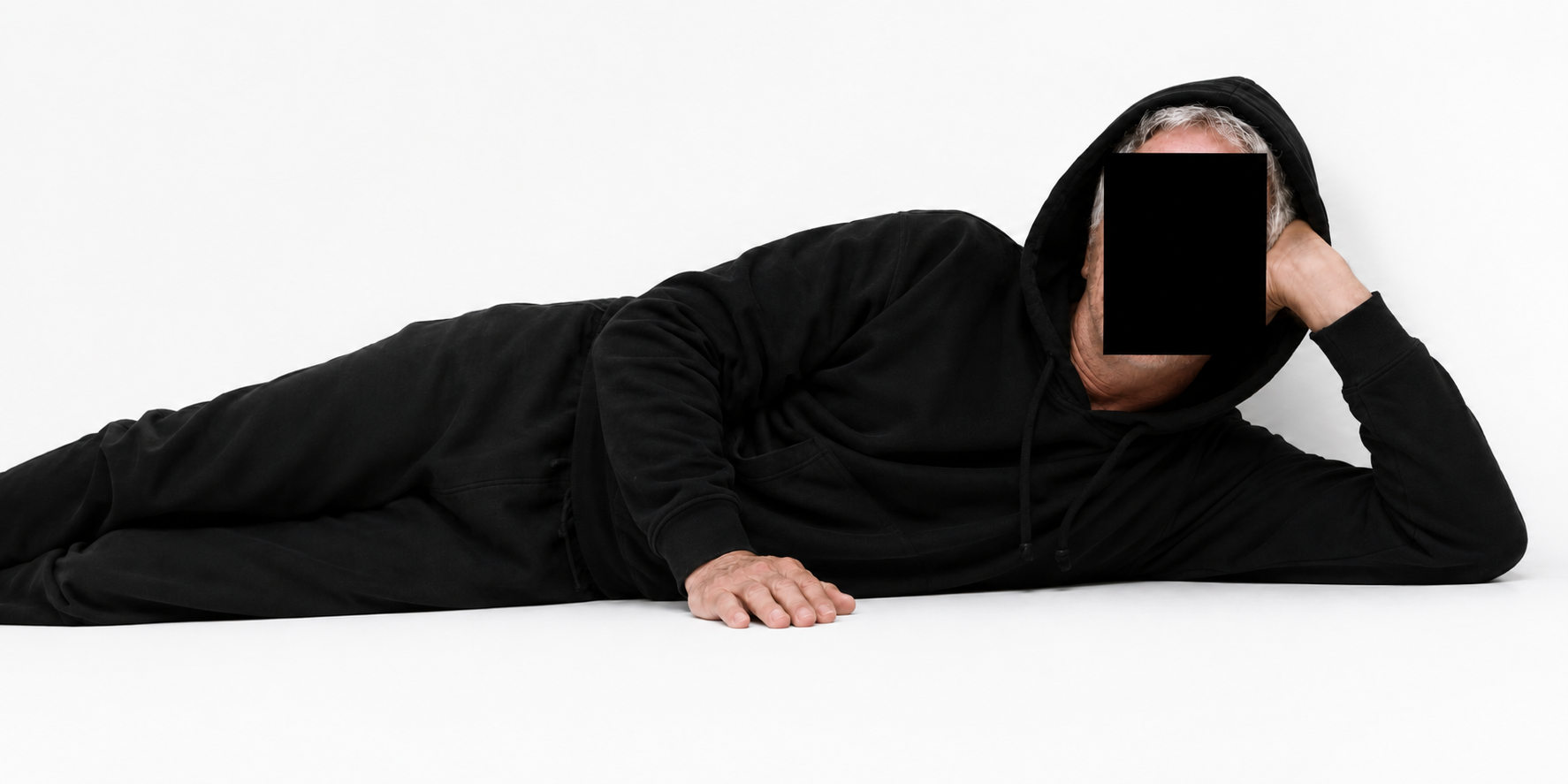 Hoodstein lying down fully at rest in an all-black hooded set
